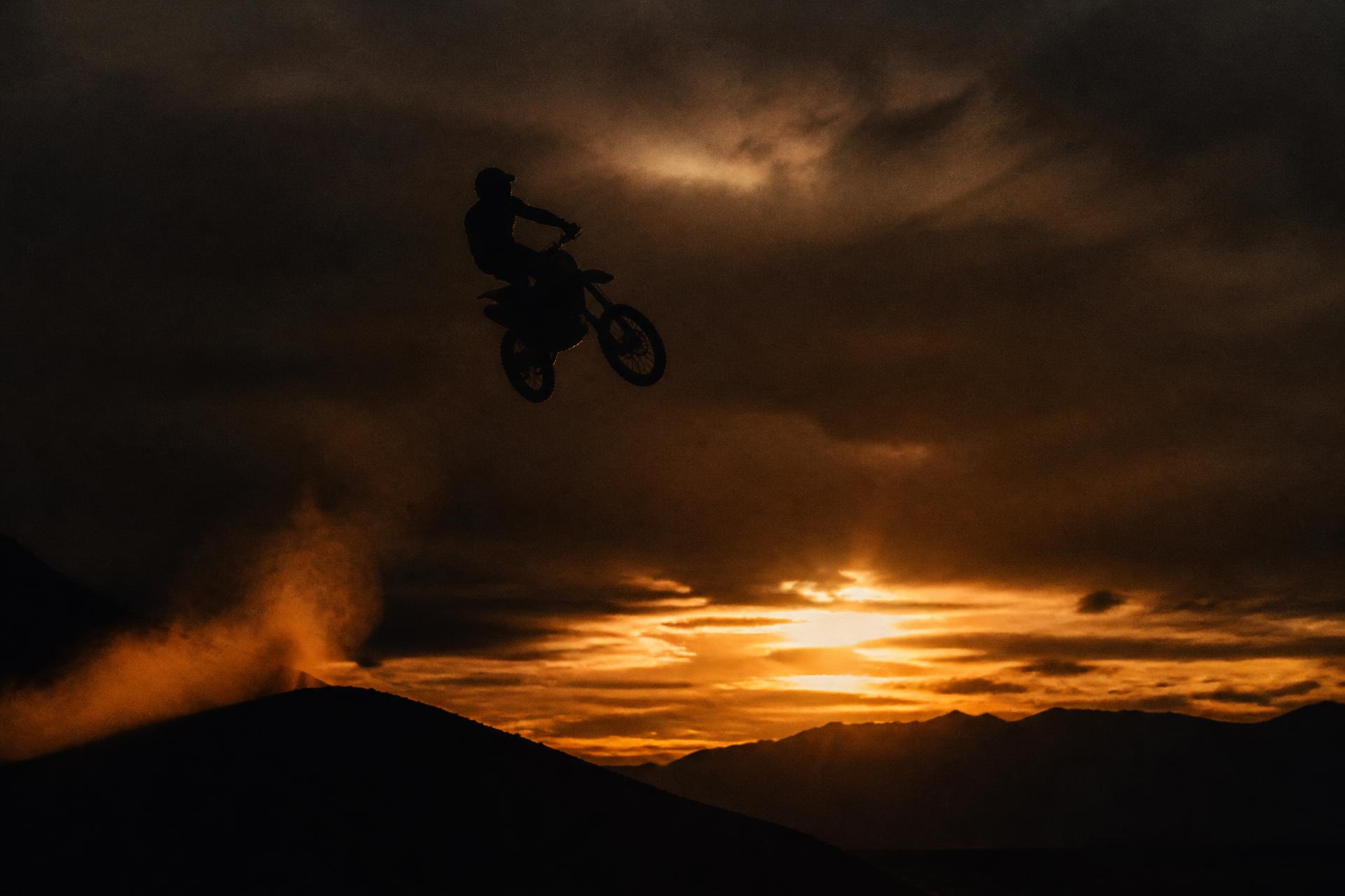 Piloto de motocross em pleno salto recortado contra o céu no fim da tarde